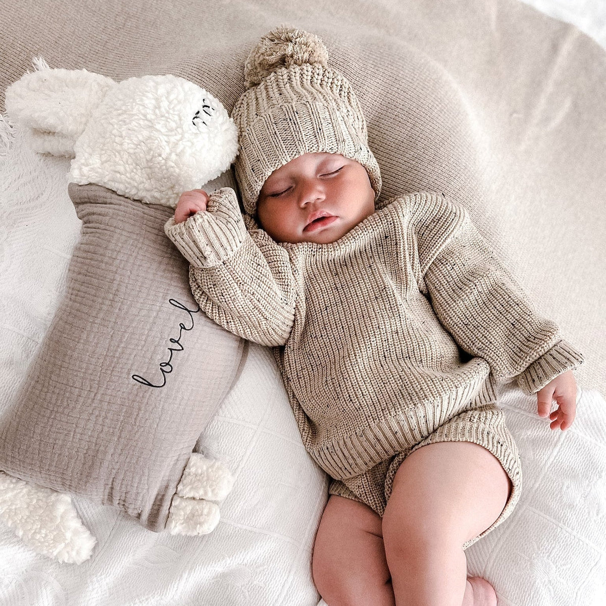 Schlafendes Baby mit Strickmütze neben einem personalisierten Kuschelschaf.