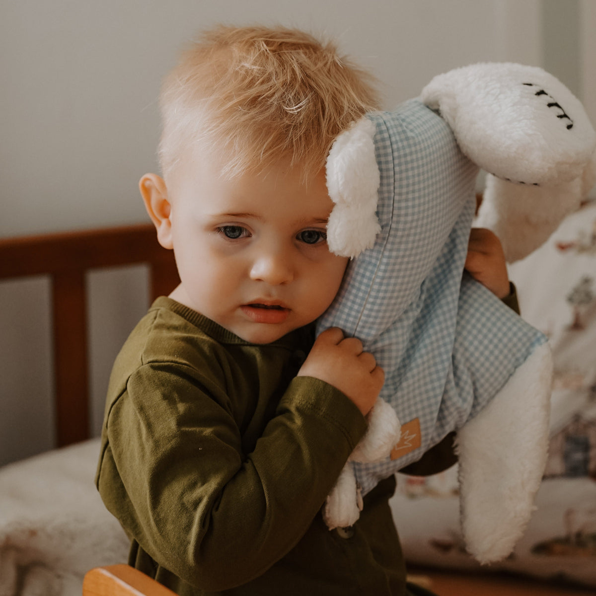 Kleinkind hält ein hellblaues Kuschelschaf neben seinem Gesicht.