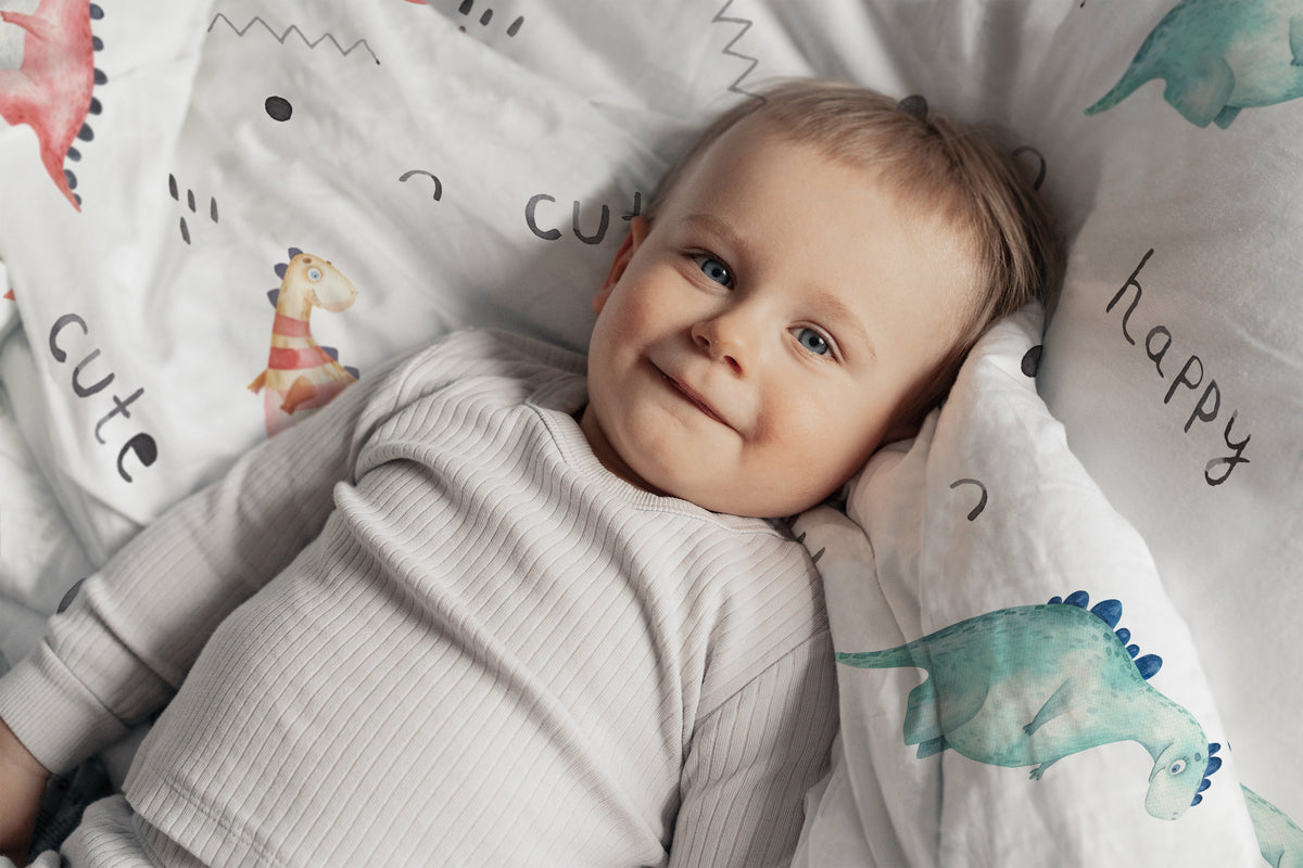 Baby liegt auf einem Kissen der Leslis-Kinderbettwäsche „Little Dino“.