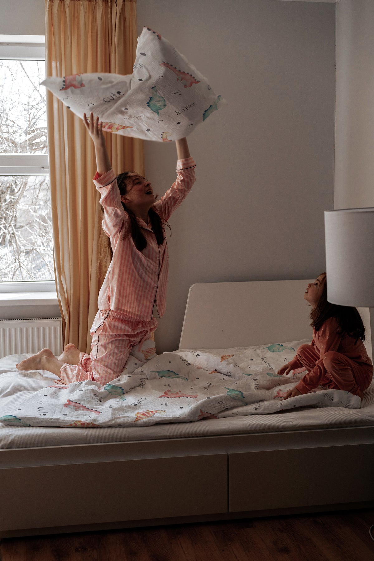 Zwei Kinder spielen mit Leslis-Kinderbettwäsche „Little Dino“ im Bett neben einem Fenster.
