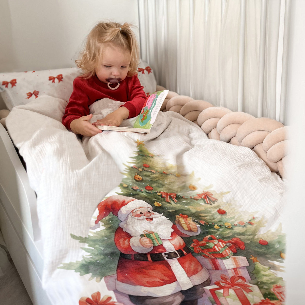 Kleinkind schaut ein Buch im Bett mit Leslis-Kinderbettwäsche „Weihnachtsmann“ an.