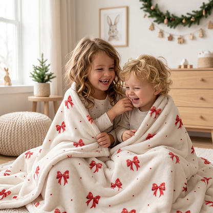 Zwei Kinder kuscheln gemeinsam unter der Kuscheldecke „Schleifen“ auf dem Sofa.